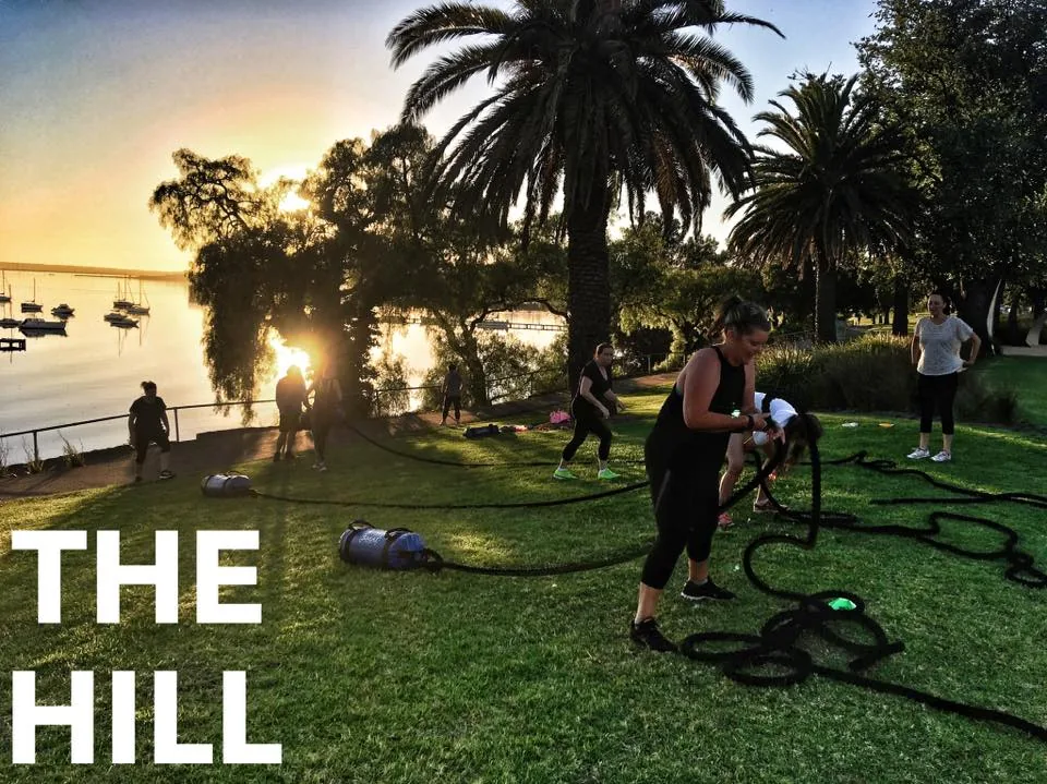 Members training with ropes and sandbags on a grassy hill by the bay